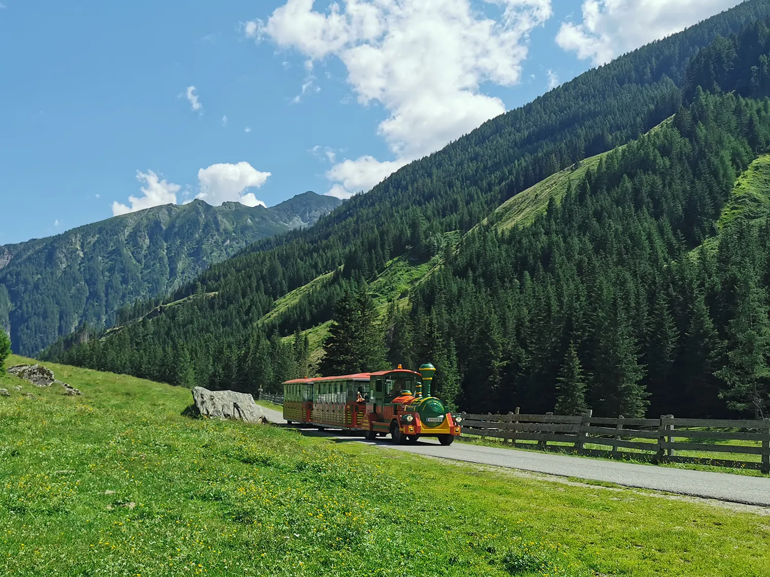 Rot-grüne Retro-Tschu-Tschu-Bahn fährt auf Straße ins Tal.